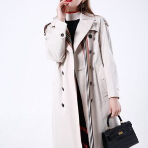 A long, double-breasted women’s trench coat featuring multi-colored vertical rainbow stripes, a unique double-belted waist, and relaxed raglan sleeves.