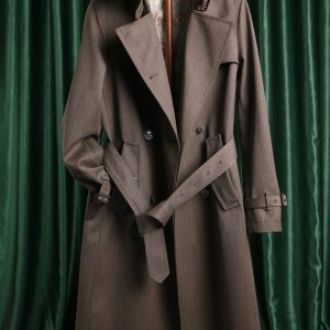 A midi-length, double-breasted women’s trench coat in 100% wool featuring a belted waist, storm flaps, and a turn-down collar.