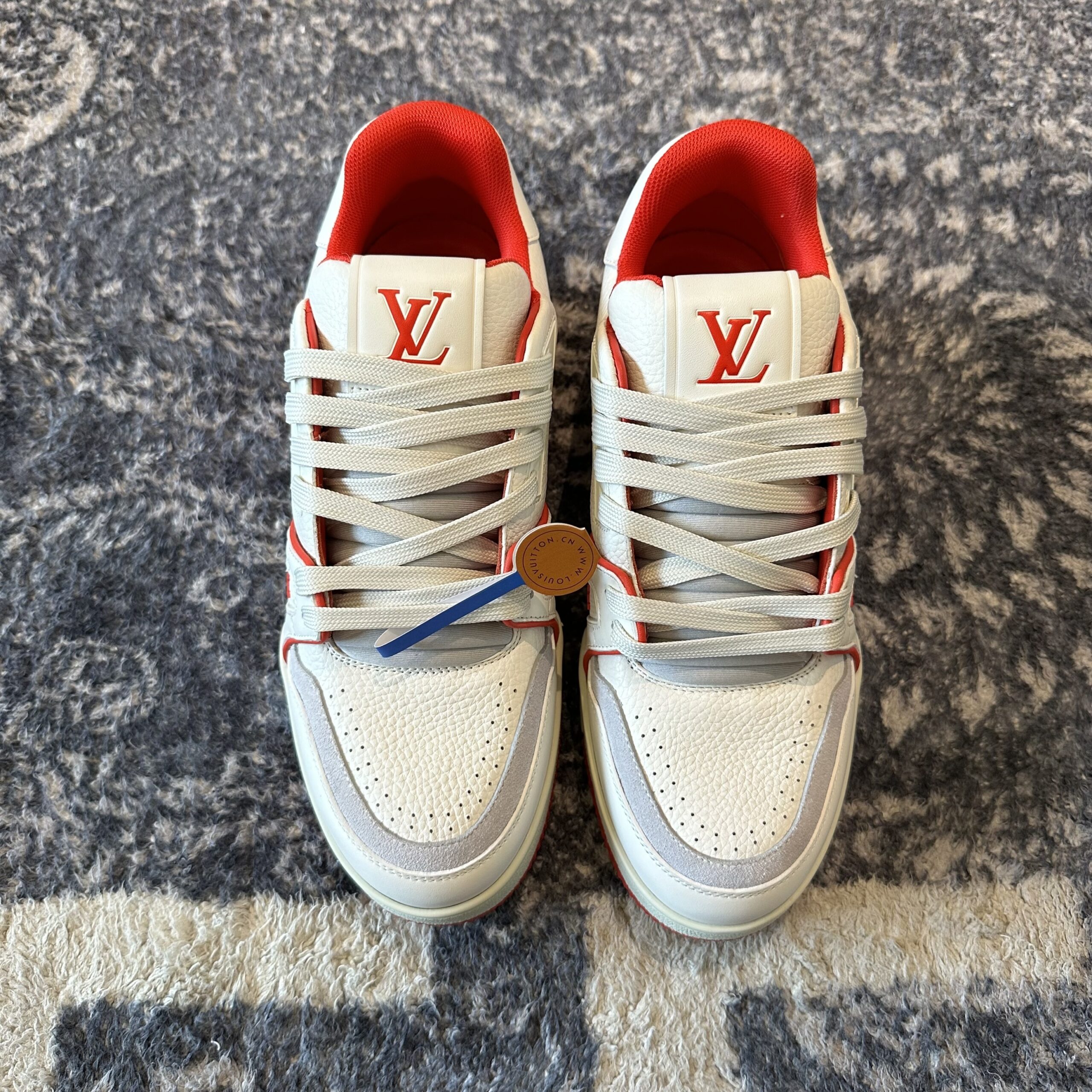 Profile view of Louis Vuitton LV Trainer in white grained leather with red piping and script signature on the side