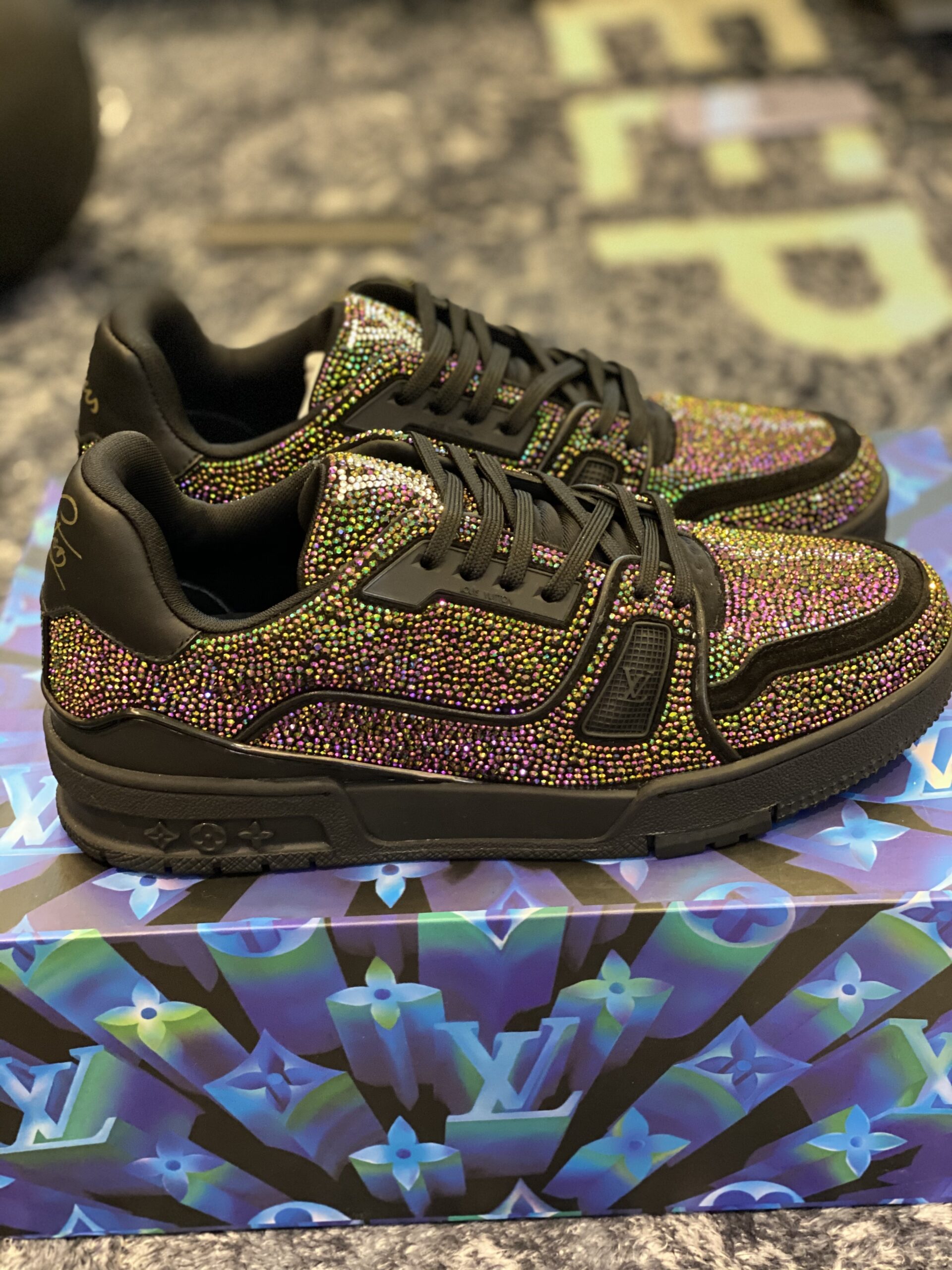 Side view of Louis Vuitton LV Trainer Black Strass sneakers covered in multicolour crystals, resting on a blue Monogram patterned box.