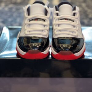 Overhead view of a pair of Air Jordan 11 Low inspired sneakers on a rug next to a black shoe box with a red "JORDAN" logo.