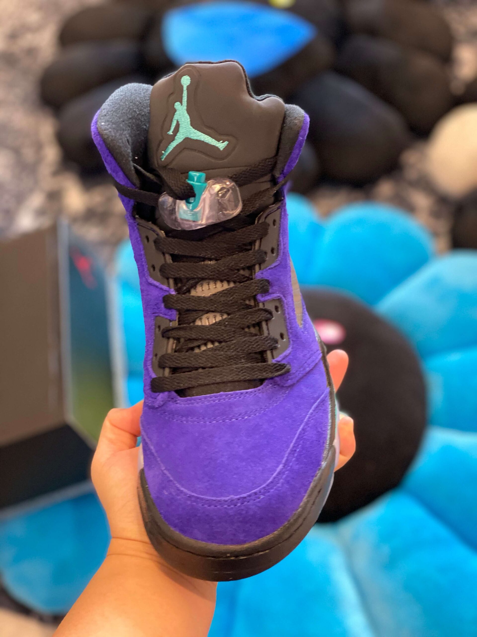 Hand holding the heel of the Air Jordan 5 Alternate Grape showing the purple suede and black Jumpman logo.