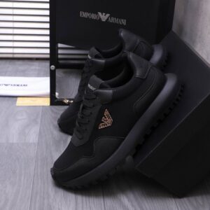 Side profile of Armani Black Sneakers showcasing the gold eagle logo, matte black upper, and thick black treaded sole on a grey floor.