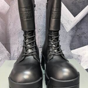 front view of black leather Balenciaga Hummer boots with a thick toothed sole and various silver charms attached to the laces.