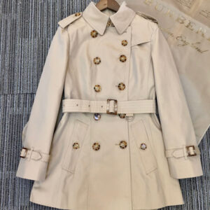 Short beige double-breasted trench coat with tortoiseshell buttons, a belted waist, cuff straps, and a plaid-patterned interior lining.
