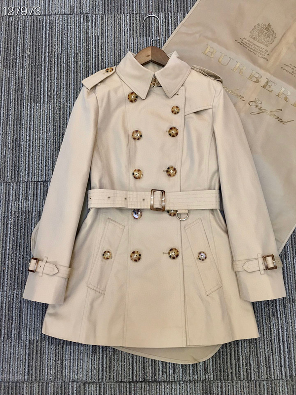 Short beige double-breasted trench coat with tortoiseshell buttons, a belted waist, cuff straps, and a plaid-patterned interior lining.