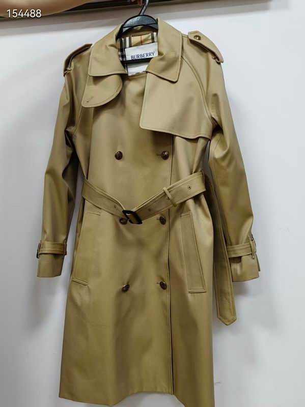 Short beige double-breasted trench coat for women with prominent tortoiseshell buttons, a belted waist, and a classic plaid-patterned interior lining.