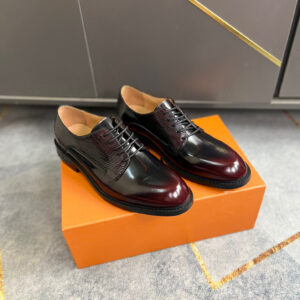 A pair of luxury brown Damier Ebene wingtip Oxford shoes with mahogany glazed leather toe caps resting on a tan designer box.