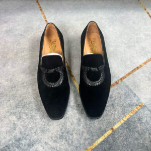 A pair of luxury black suede sneakers with braided Gancini buckle detailing resting on a grey floor.