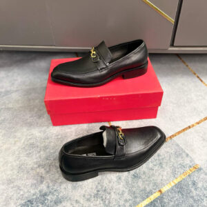 A pair of luxury black suede loafers with hand-braided leather Gancini details resting on a vibrant red designer shoe box.