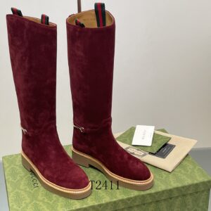 Pair of tall burgundy suede boots with gold horsebit hardware and tan rubber soles on a green logo box.