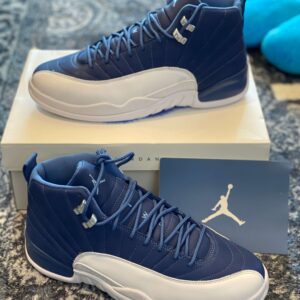 Three-quarter profile view of two Air Jordan 12 Retro sneakers, one sitting on the box and one in front, showing the Navy and White colors.