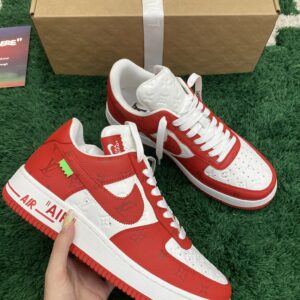 Side view of LV X NIKE AIR FORCE 1 LOW RED WHITE sneakers with red monogram leather overlays and white debossed panels on a green grass-textured rug.