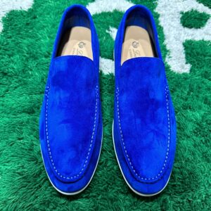 Pair of luxury Loro Piana Summer Walk loafers in royal blue suede with white rubber soles on a green textured background.