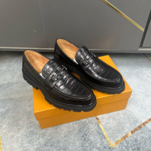 Pair of black croc-embossed Louis Vuitton loafers with a thick lug sole and dark metal bit hardware on a yellow box.