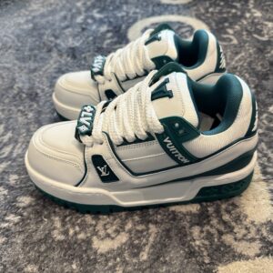 Side profile of two Maxi Trainer sneakers in white and green resting on a patterned grey carpet.