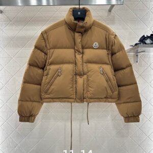 A front view of the Moncler Brown Crop Puffer Jacket hanging on a rack against a white textured wall.