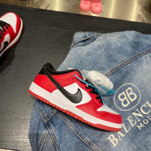 Side profile of Nike Red/White/Black SB Dunk Low sneakers resting on a denim surface.