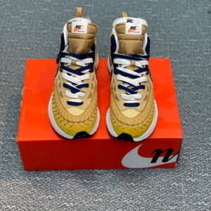 A pair of Nike Sesame Yellow VaporWaffle Shoes featuring tan suede, yellow accents, and unique baseball stitching displayed in front of an orange box.