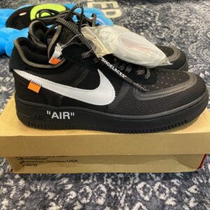 Pair of OFF-WHITE x Nike Air Force 1 Low inspired sneakers in Black and White, showcasing the stitched Swoosh and "AIR" text on the midsole, next to a brown shoe box.