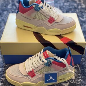 Side view of the Union LA x Air Jordan 4 Retro Guava Ice showing the pink suede, blue eyelets, and yellow UN/LA tag.