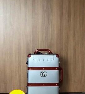 Front view of the Gucci Silver and Red Rolling Suitcase with red leather-style straps and gold interlocking logo.