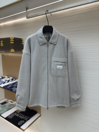 A front-view studio shot of a CD-logo Light Grey Fleece Overshirt hanging on a black hanger against a white textured wall. The overshirt features a full-length silver zipper, a classic collar, and a unique zippered chest pocket adorned with a white "Christian Dior" brand patch. In the background, a luxury boutique setting is visible, including a Louis Vuitton monogram trunk and folded designer knitwear on glass shelving.
