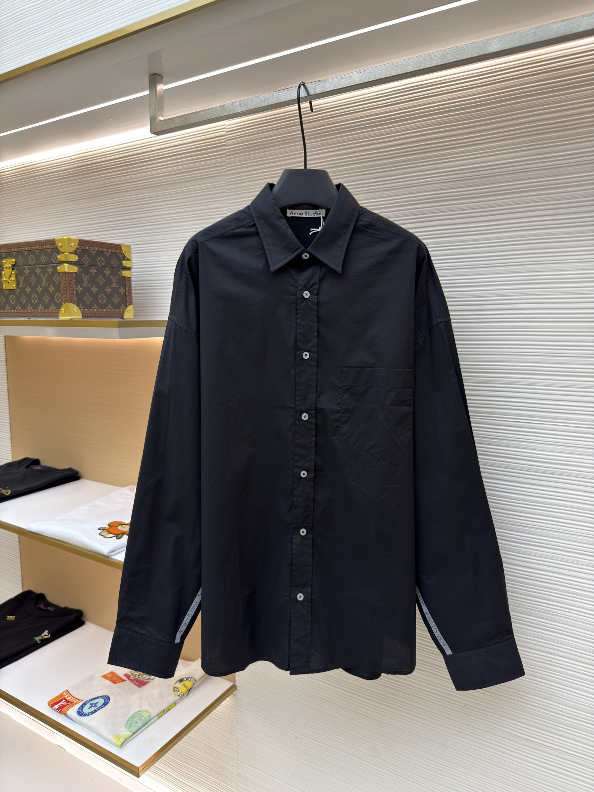 Front view of the Acne Studios Black Oversized Shirt hanging in a luxury retail setting.