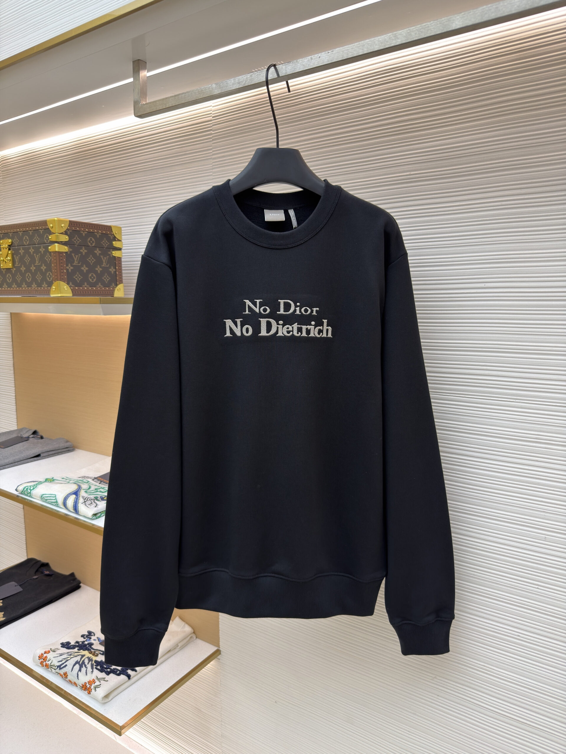 A premium Dior Black Slogan Sweatshirt featuring silver-grey embroidery hanging in a luxury closet setting.