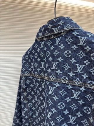 Premium dark blue Louis Vuitton Monogram Denim Jacket featuring the iconic LV monogram pattern throughout. Classic trucker-style denim jacket with branded silver buttons hanging in a high-end boutique display.