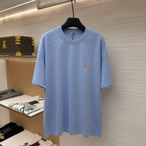 A vibrant Moncler Blue Graphic T-Shirt with a colorful abstract logo print on the chest hanging in a luxury store.