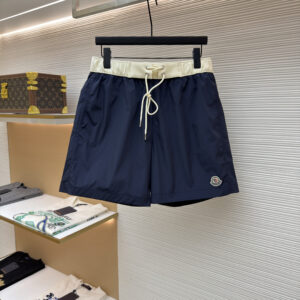 A pair of Moncler Navy Blue Swim Shorts with a cream waistband and logo patch hanging on a display rack.