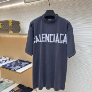 A men's Balenciaga dark grey oversized washed cotton t-shirt with a white block logo hanging on a clothes rail.