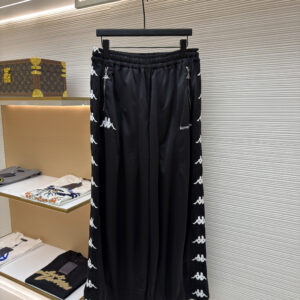 Front view of Acne Studios x Kappa Black Trackpants featuring embroidered dual branding and side logo taping on a display hanger.