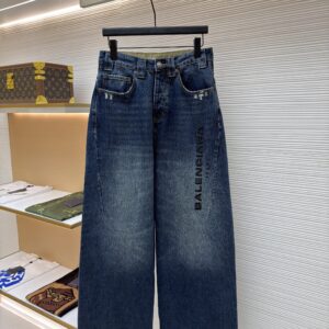 A pair of dark blue Balenciaga wide-leg jeans hanging on a black hanger in a luxury boutique.