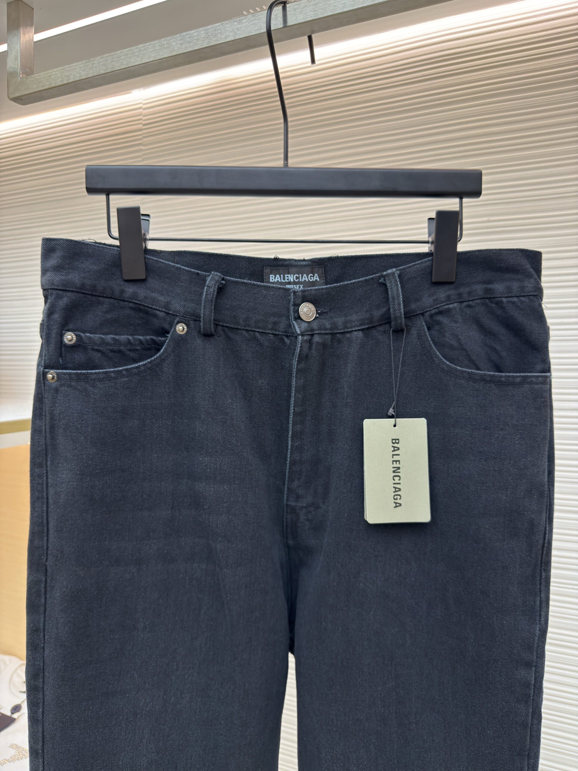 Front and back view of washed black Balenciaga flared denim jeans hanging on a display