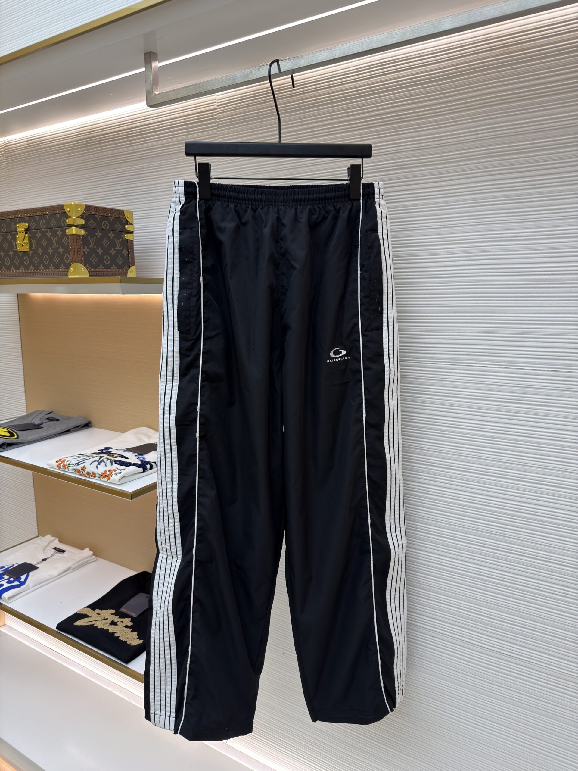 A pair of black Balenciaga oversized track pants with white side stripes hanging in a luxury boutique