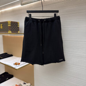 A pair of premium Celine Black Raw-Hem Fleece Shorts in black, hanging on a black hanger, showcasing the white logo on the leg and the raw-cut hem.