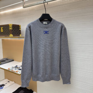 A high-quality slate grey knit sweater with a royal blue embroidered logo on the chest, shown in a boutique display.
