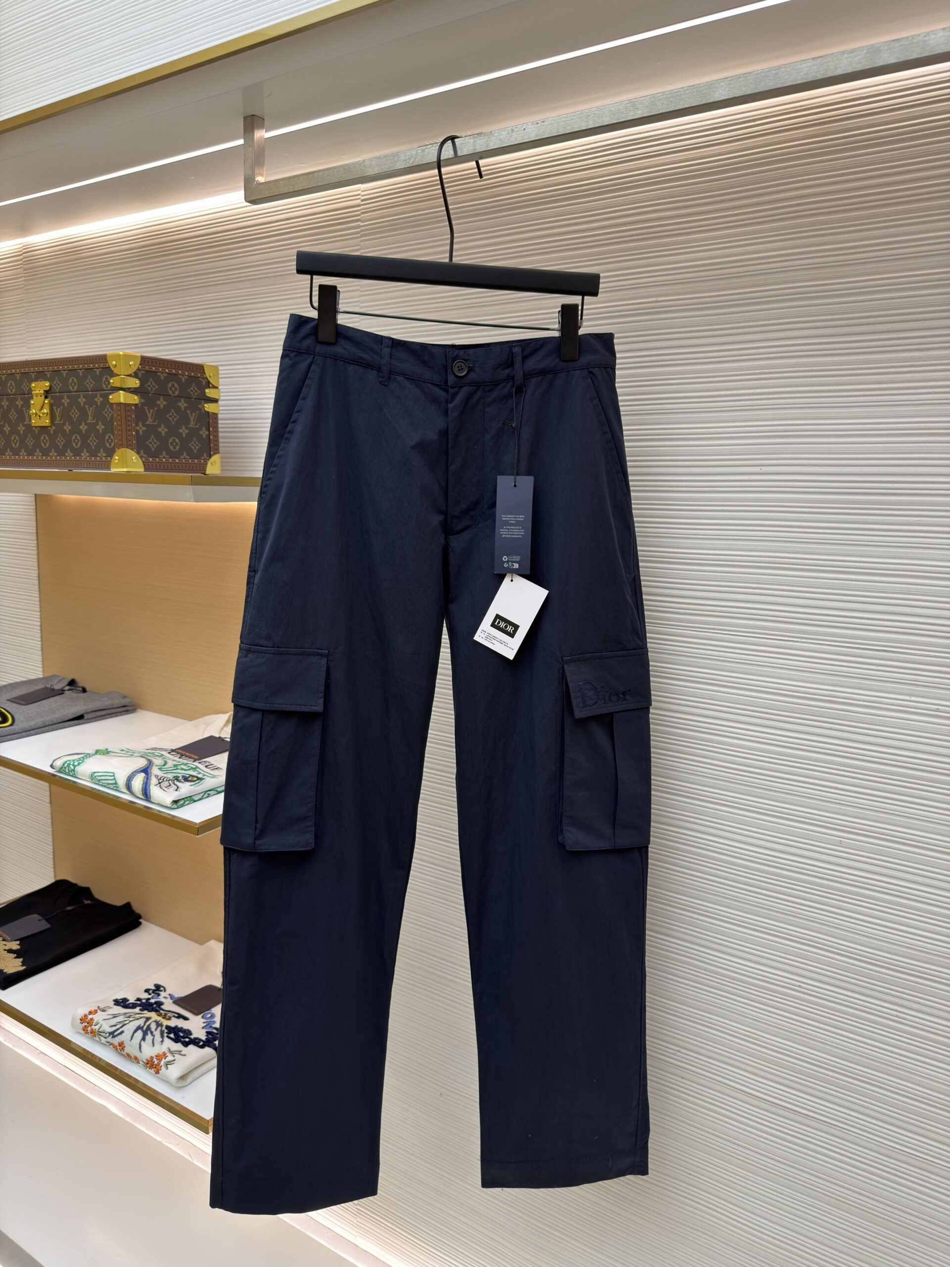 A pair of Dior Navy Cargo Trousers hanging on a black hanger, showing the front and back views including the cargo pockets and logo details.
