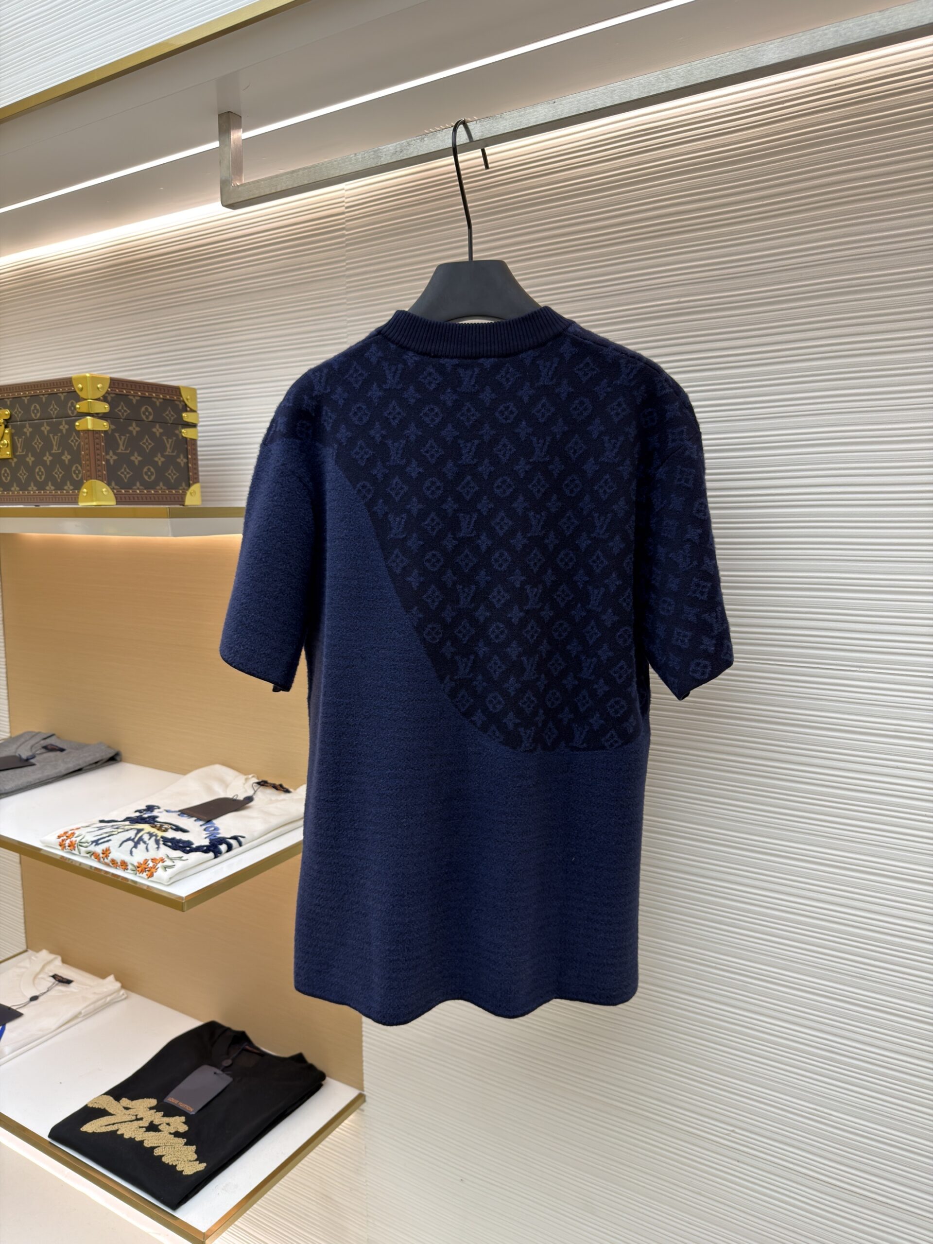 A navy blue knit t-shirt with a diagonal monogram wave pattern on the chest and shoulder hanging on a luxury display rack.