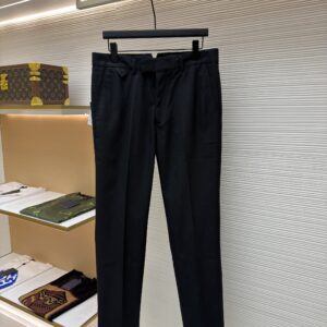 Front and back view of black Louis Vuitton formal trousers with a tonal Damier pattern hanging on a display