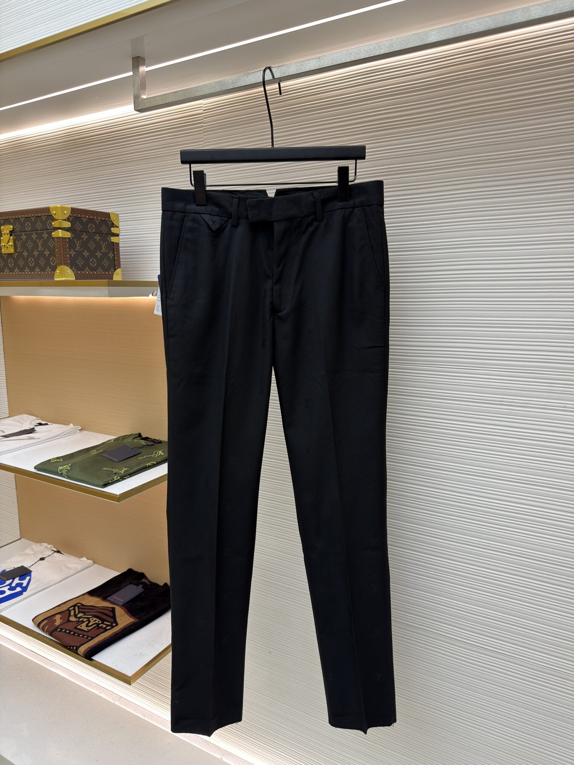Front and back view of black Louis Vuitton formal trousers with a tonal Damier pattern hanging on a display