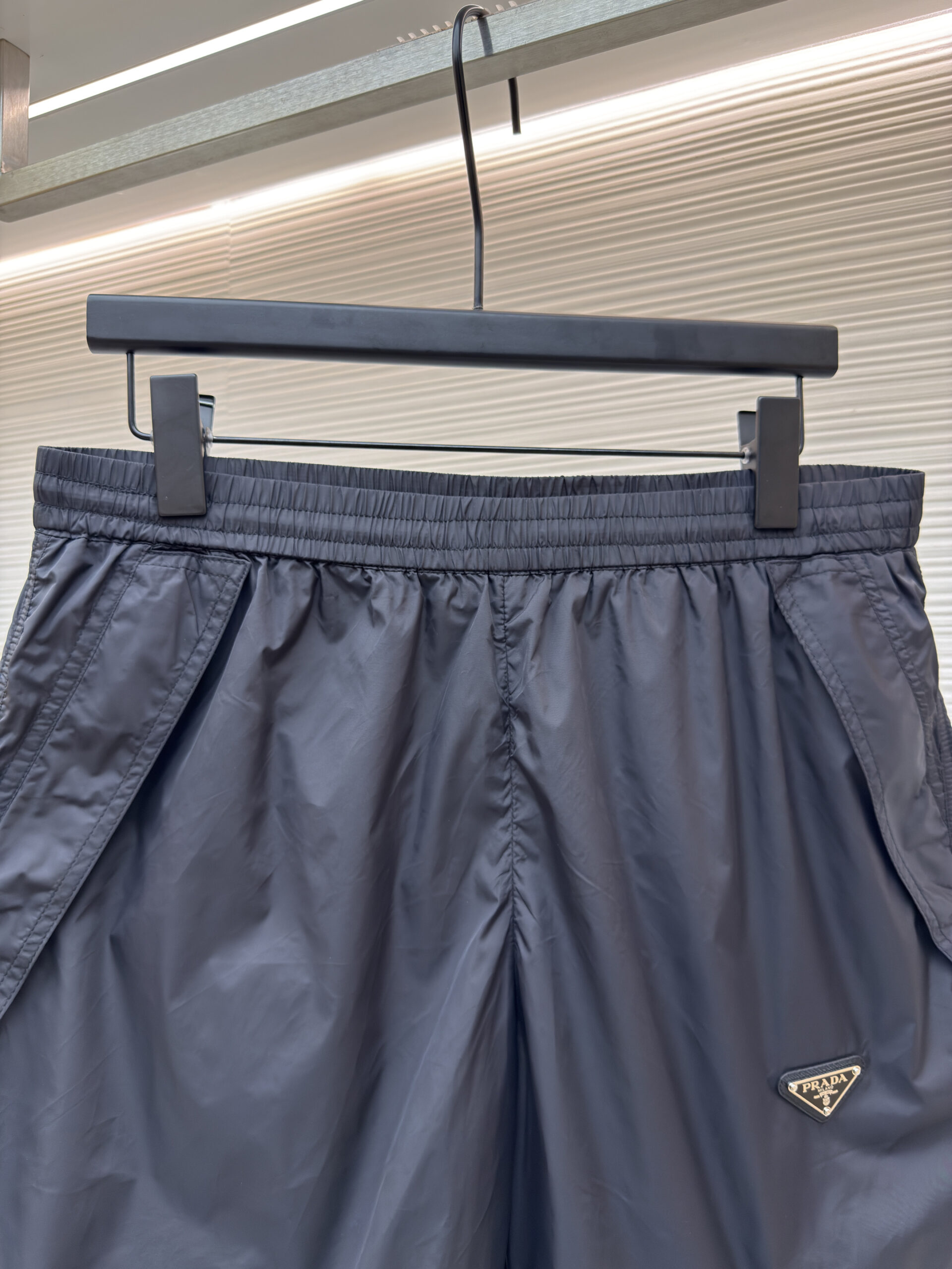 Front view of black Prada technical nylon shorts featuring an enameled triangle logo hanging on a display rack.
