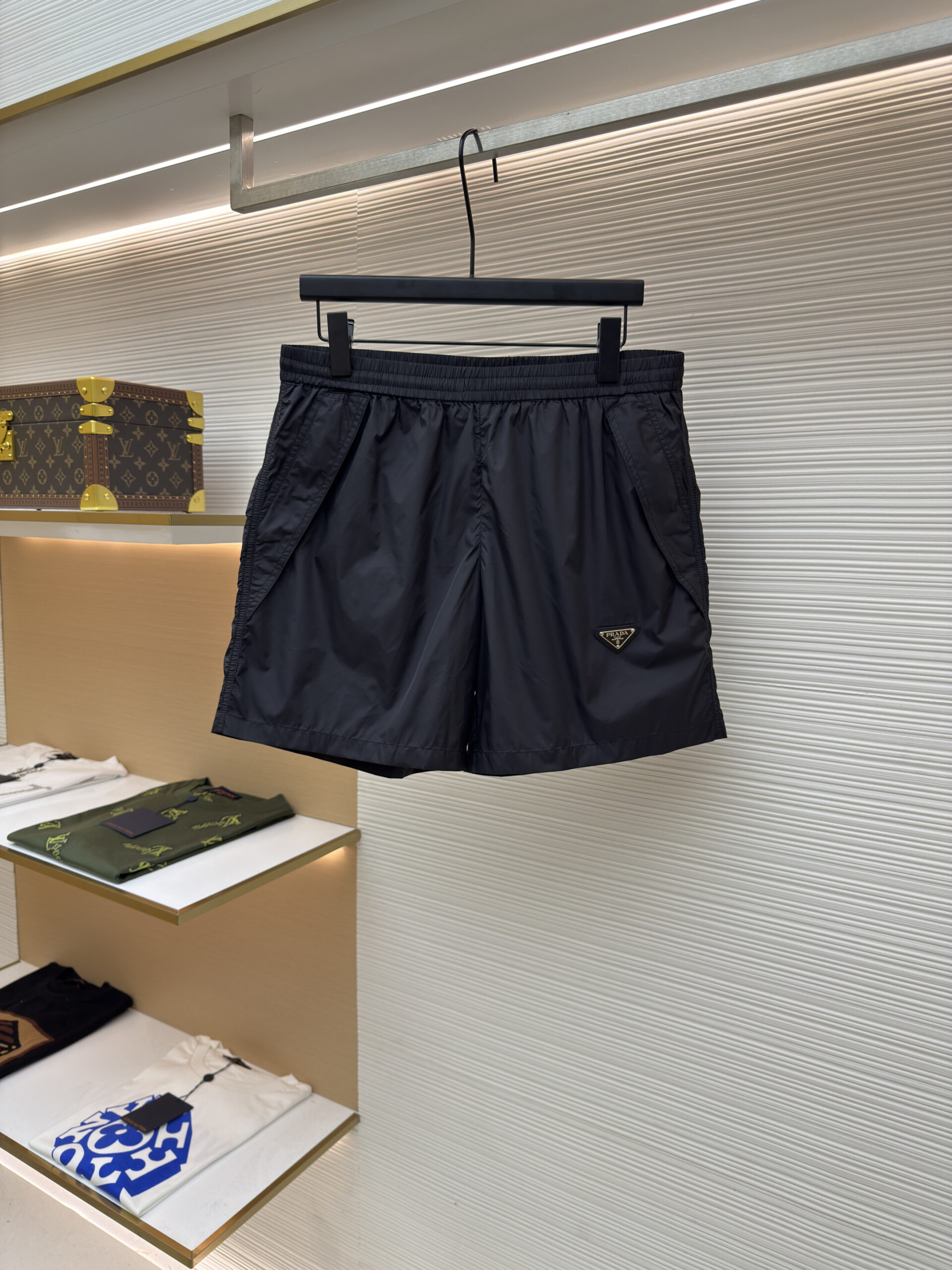 Front view of black Prada technical nylon shorts featuring an enameled triangle logo hanging on a display rack.