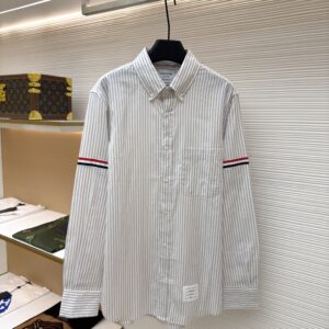 Front view of a grey and white striped Thom Browne long-sleeved shirt with tricolour armbands hanging on a display.