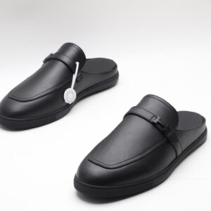 Hermès monochromatic black leather slip-on mules with an apron toe and black rubber soles on a white background.