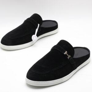Hermès black suede slip-on mules with an apron toe and white rubber soles on a white background