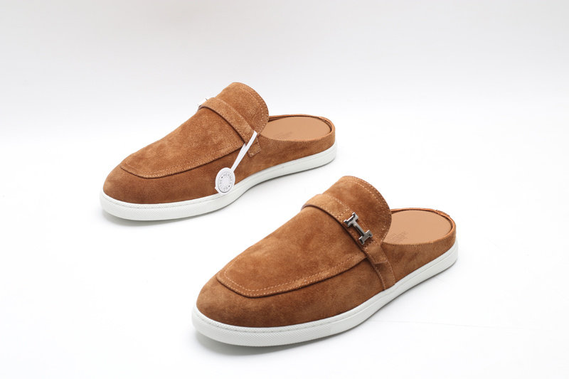 Tan suede slip-on mules with an apron toe and white rubber soles on a white background.