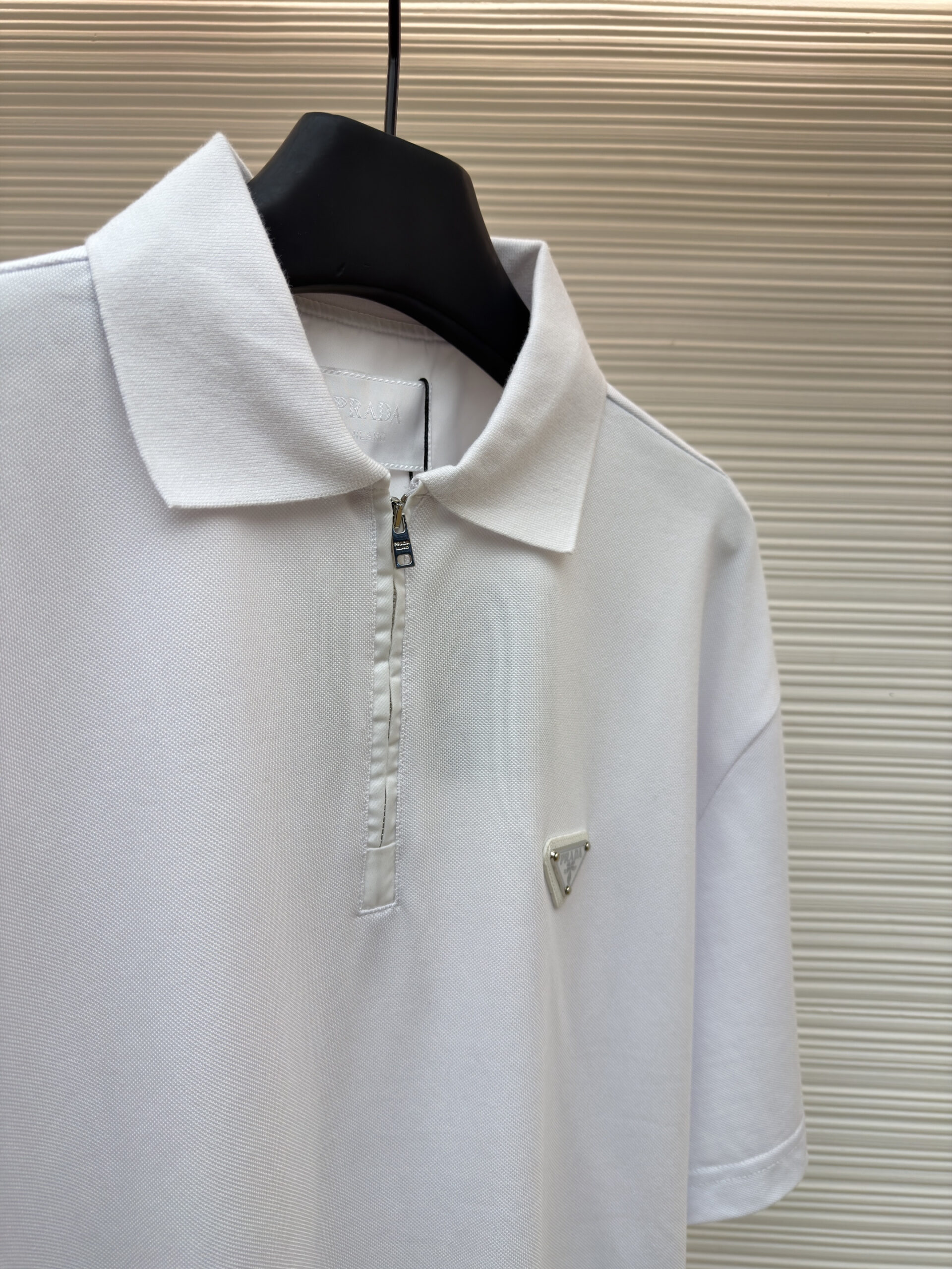 Front and back view of the premium Prada Logo Charm Beige Chino Trousers hanging on display, showcasing the tailored leg crease and rear buttoned pockets.
